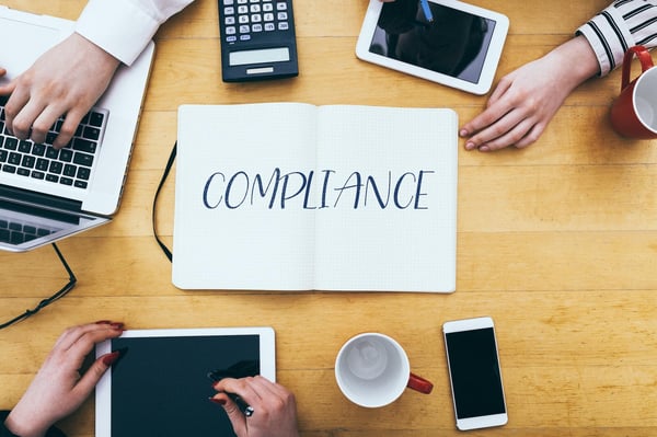 compliance-headline-on-paper-notebook-at-small-business-office-desk-with-young-adult-workers